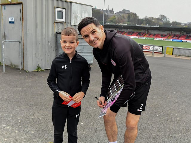 Derry City’s Ciaran Coll signs a photograph for Finley Bradley, age 8, on Saturday morning prior to the team’s departure for Dublin ahead of Sunday’s FAI Cup Final against Drogheda United. Photograph: George Sweeney.