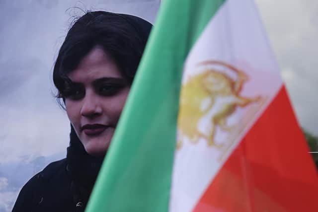 A portrait of Mahsa Amini stands next to an Iranian opposition flag during a protest gathering of supporters of the National Council of Resistance of Iran, an Iranian opposition group based abroad, on September 28, 2022 in Berlin, Germany. Amini, 22, was arrested by Iranian authorities in Tehran on September 13, 2022, for not wearing her headscarf properly and died three days afterwards, apparently due to a severe head injury. Her death has sparked demonstrations in Iran nationwide that have spiralled into violence between protesters and police and left dozens of protesters dead. (Photo by Sean Gallup/Getty Images)