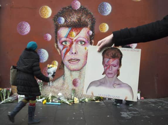 A man holds David Bowie's album Aladdin Sane in front of a mural of Bowie on the wall of a Morley's store in Brixton, London, the singers birthplace, after the rock star died following an 18-month battle with cancer. PRESS ASSOCIATION Photo. Picture date: Monday January 11, 2016. See PA story DEATH Bowie. Photo credit should read: Anthony Devlin/PA Wire