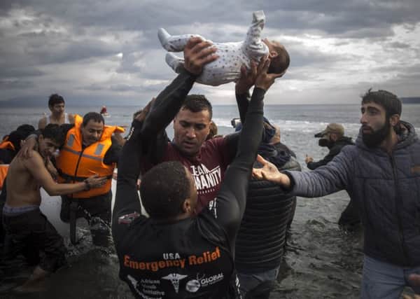 A volunteer holds up a baby as others help migrants and refugees to disembark from a dinghy after their arrival from the Turkish coast to the Greek island of Lesbos. (AP Photo/Santi Palacios)