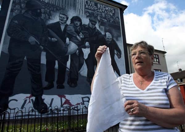 Kay Duddy, the sister of Jackie Duddy who was shot dead on Bloody Sunday, pictured in 2010, standing in front of a mural depicting the moment her brother was led away from danger by Edward Daly as she holds the white handkerchief that Father Daly waved as he did so.